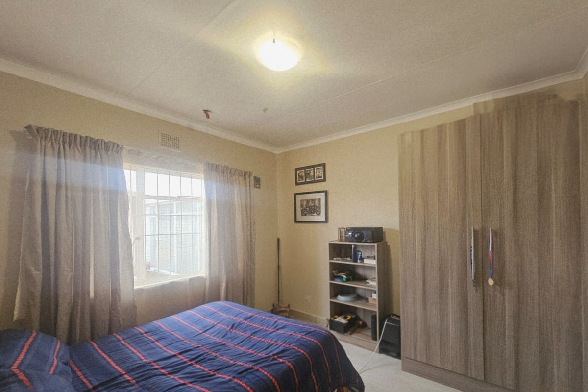 A functional bedroom featuring a built-in wooden wardrobe and a window with curtain tracks.