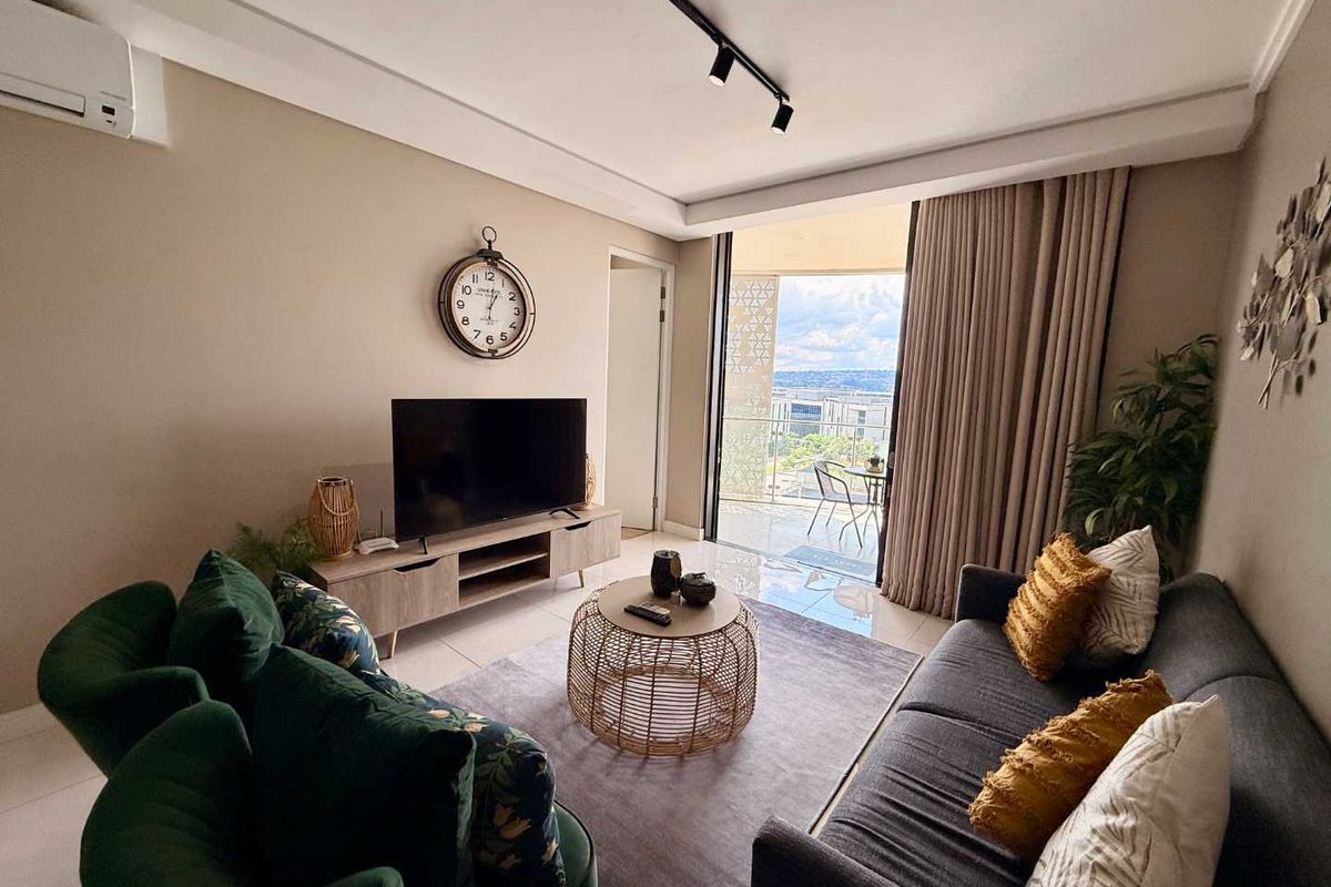 A well-maintained living room featuring modern track lighting, a wall-mounted air conditioning unit, and large sliding glass doors leading to a private balcony.