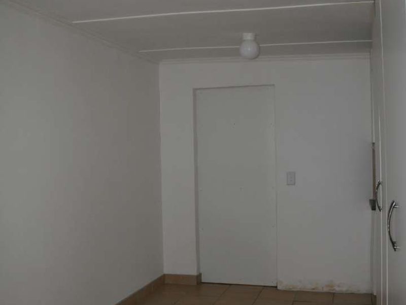 An empty hallway featuring tiled flooring, built-in cupboards, and basic ceiling lighting, showing signs of wall staining near the base.