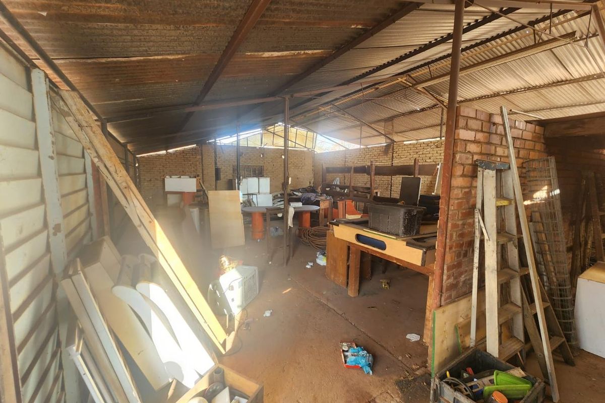 A large, industrial-style utility or workshop space featuring exposed brick walls, steel structural supports, and a corrugated iron roof.