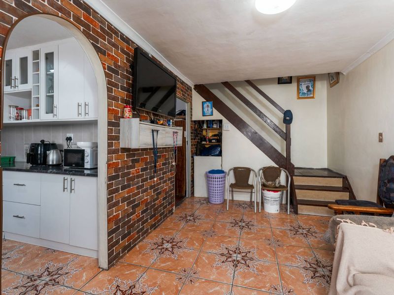 Open plan living area featuring an exposed brick wall, tiled flooring, and an arched entryway leading into a compact kitchen space with built-in cabinetry.