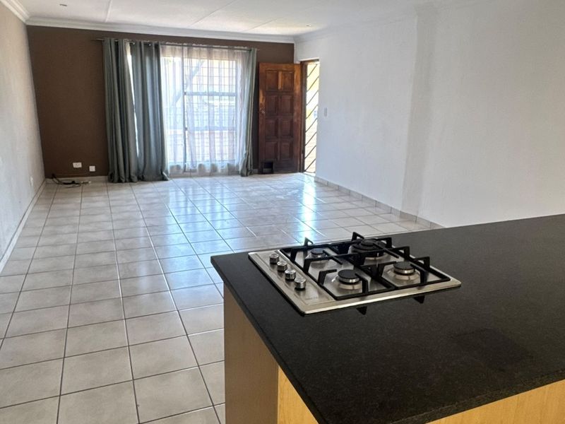 Spacious open-plan living area featuring a kitchen island with a built-in gas hob and neutral tiled flooring throughout.