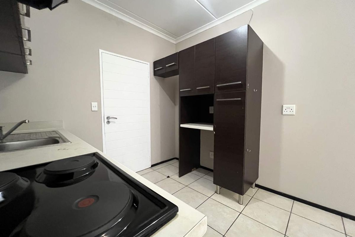 A functional kitchen area featuring dark cabinetry, a built-in electric hob, stainless steel sink, and tiled flooring.