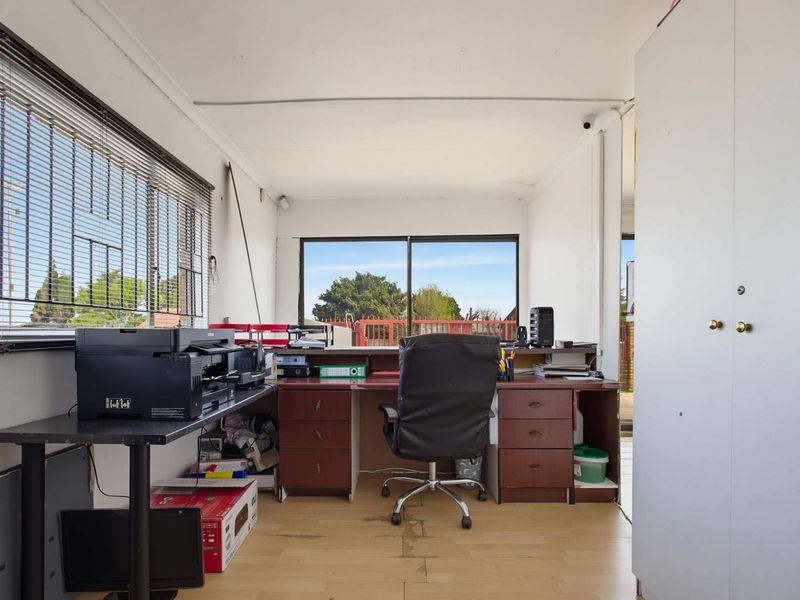 A functional home office space featuring built-in cabinetry, laminate flooring, and large windows providing natural light and outdoor access.