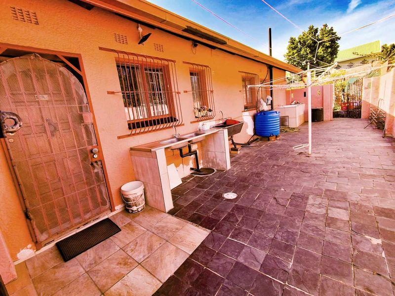 Rear exterior area featuring a paved patio, security gates, security bars on windows, and a functional outdoor sink and prep area.