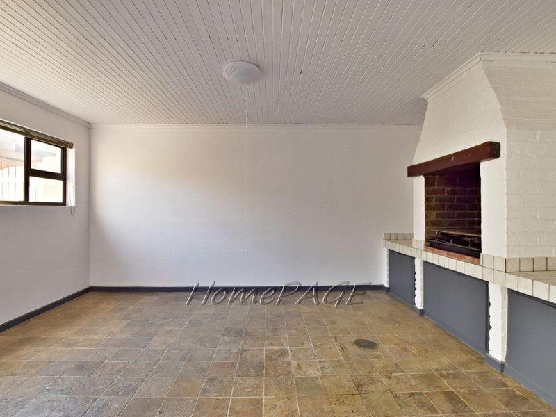 An empty covered patio area featuring a built-in brick braai, tiled flooring, and a white tongue and groove ceiling.