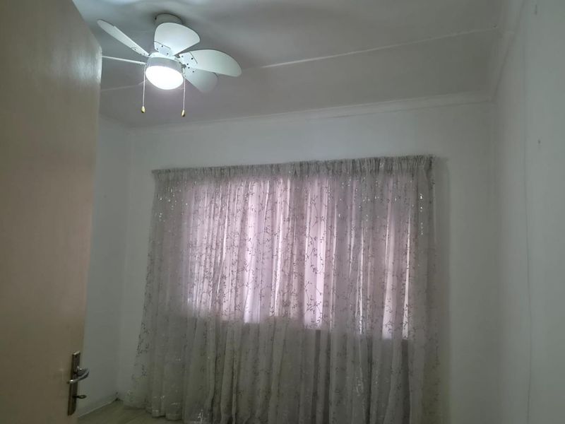 A simple, empty bedroom featuring a ceiling fan and window with curtain tracks, providing a blank canvas for personalization.