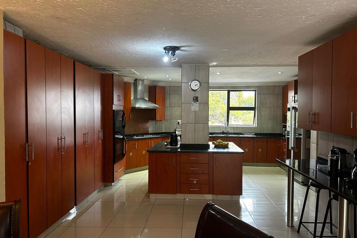 Spacious kitchen featuring dark wood cabinetry, granite countertops, a central island, built-in oven, extractor fan, and tiled flooring.