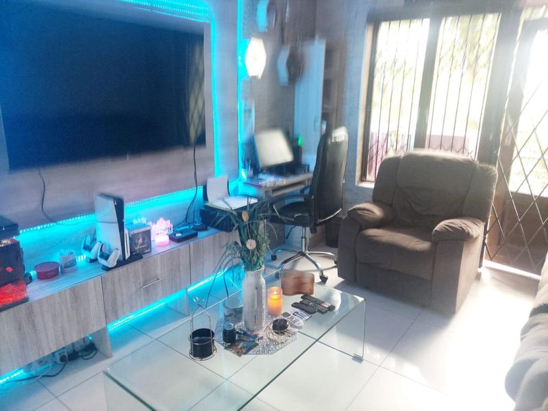 A living room featuring tiled flooring, a built-in media unit with integrated lighting, and access to an outdoor area through a security gate.