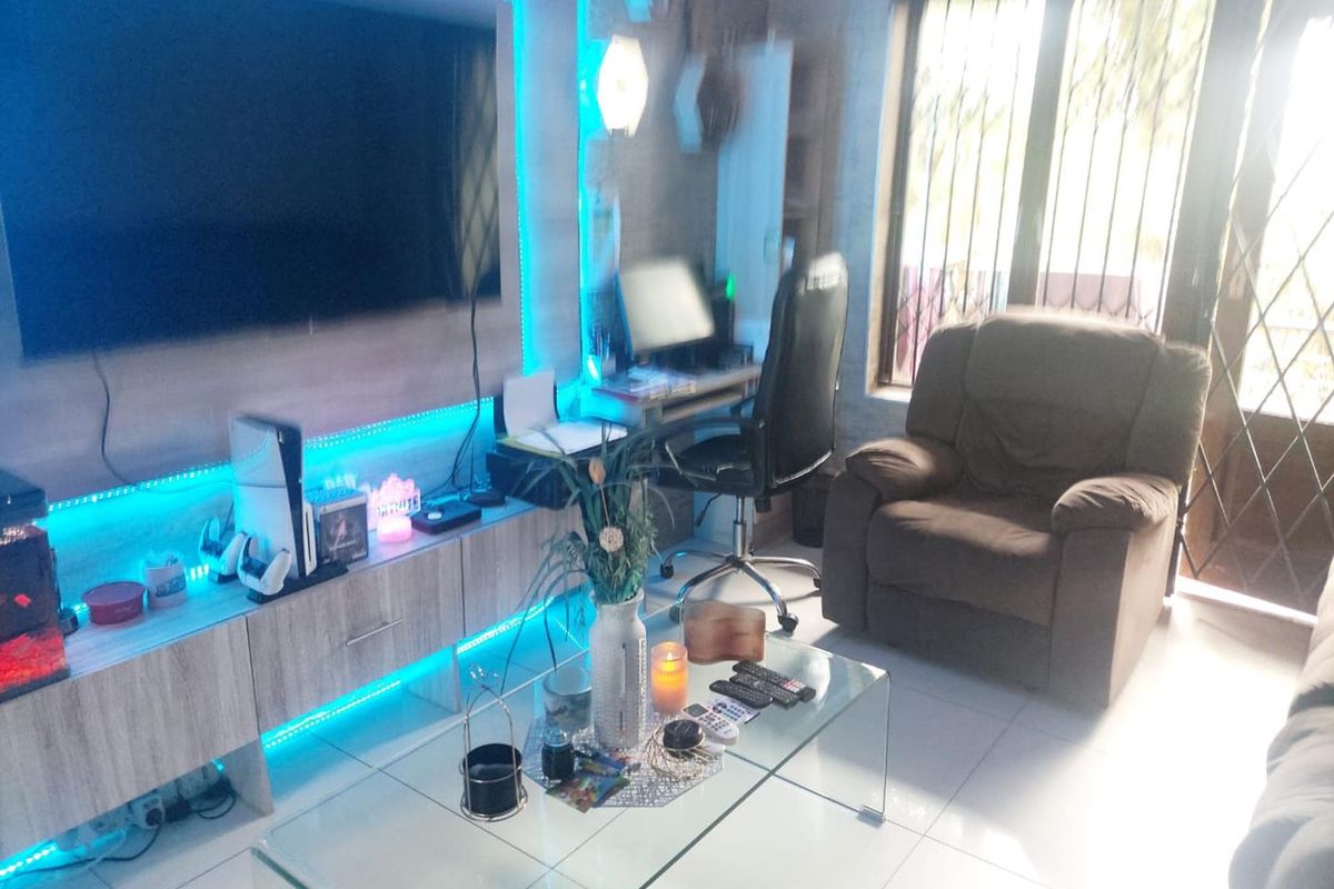 A living room featuring tiled flooring, a built-in media unit with integrated lighting, and access to an outdoor area through a security gate.