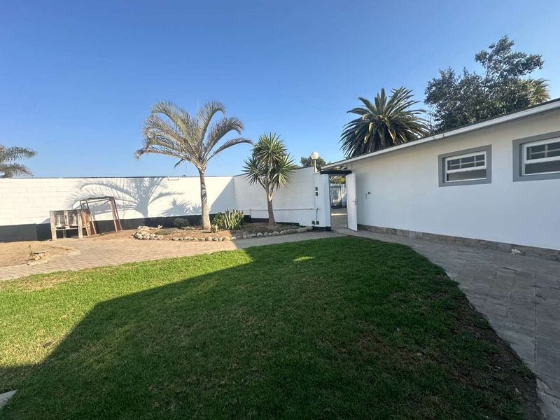 A private rear garden featuring a paved area, well-maintained lawn, and secure boundary walls, providing a clean and functional outdoor space.