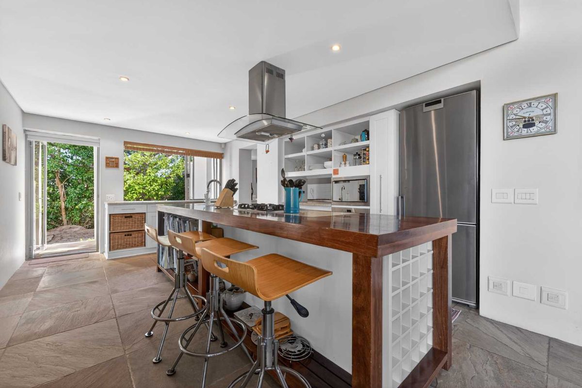 Modern kitchen featuring a large wooden island with integrated wine storage, stainless steel extractor fan, and stone tile flooring with direct outdoor access.