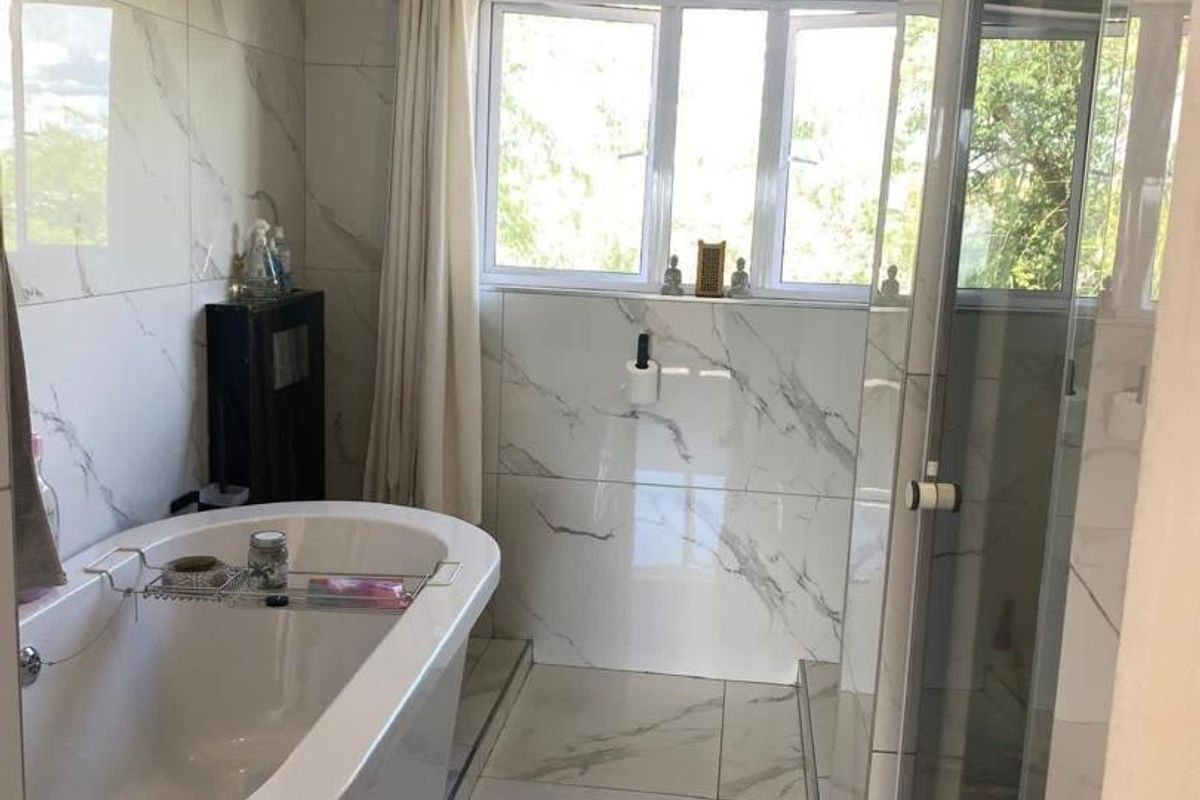 Modern bathroom featuring floor-to-ceiling marble-look tiles, a sleek freestanding bathtub, and a separate glass-enclosed shower area.