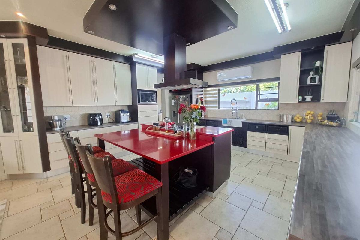 Spacious kitchen featuring a central island with a red countertop, extensive built-in cabinetry, a farmhouse sink, and a modern extractor fan.