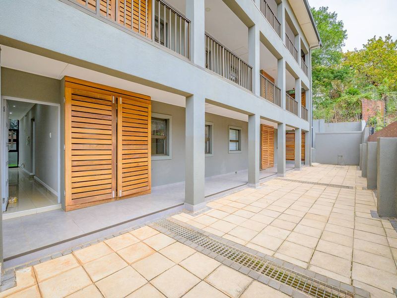 A well-maintained rear exterior area featuring a paved patio, timber slatted shutters, and multi-level balcony access with metal balustrades.