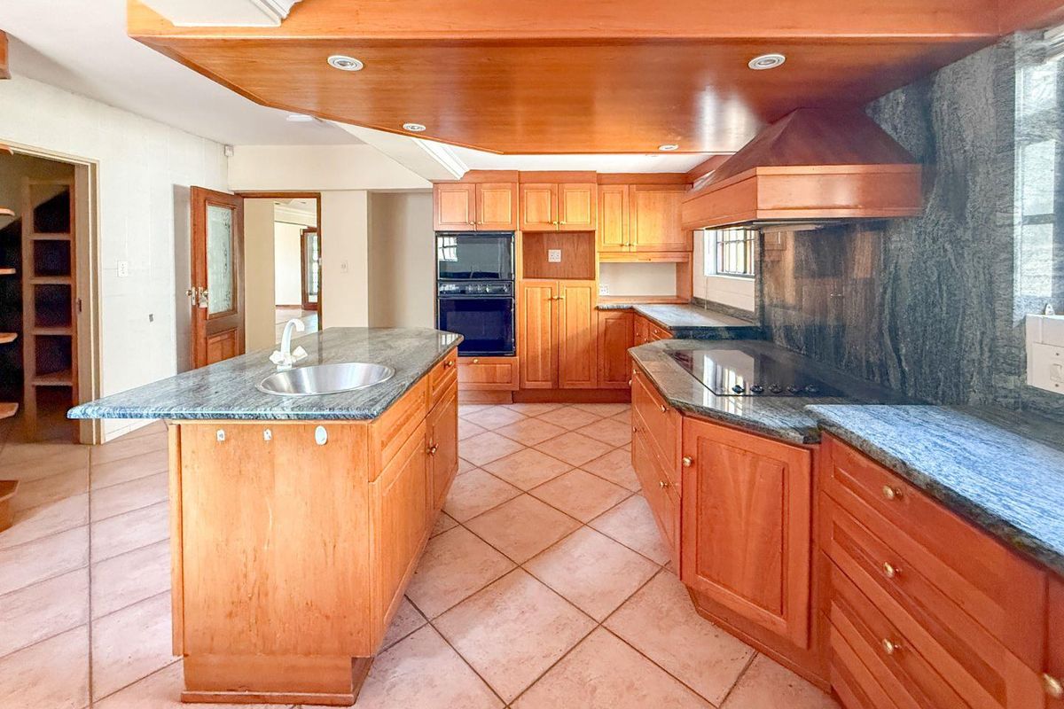 Spacious kitchen featuring timber cabinetry, granite countertops, a central island with sink, built-in oven, and a dedicated cooktop with extractor fan.