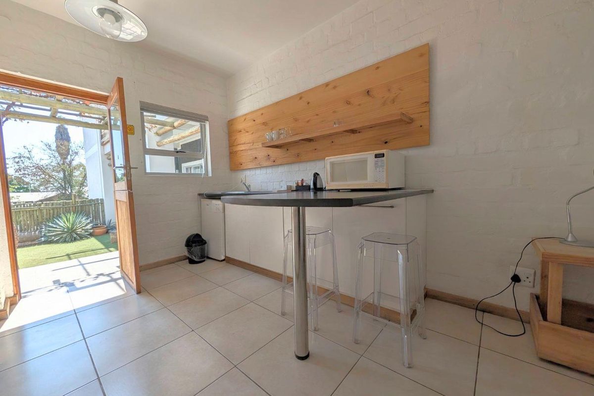 A compact kitchenette featuring built-in cabinetry, a stainless steel sink, and timber wall shelving, with direct access to an outdoor patio area.