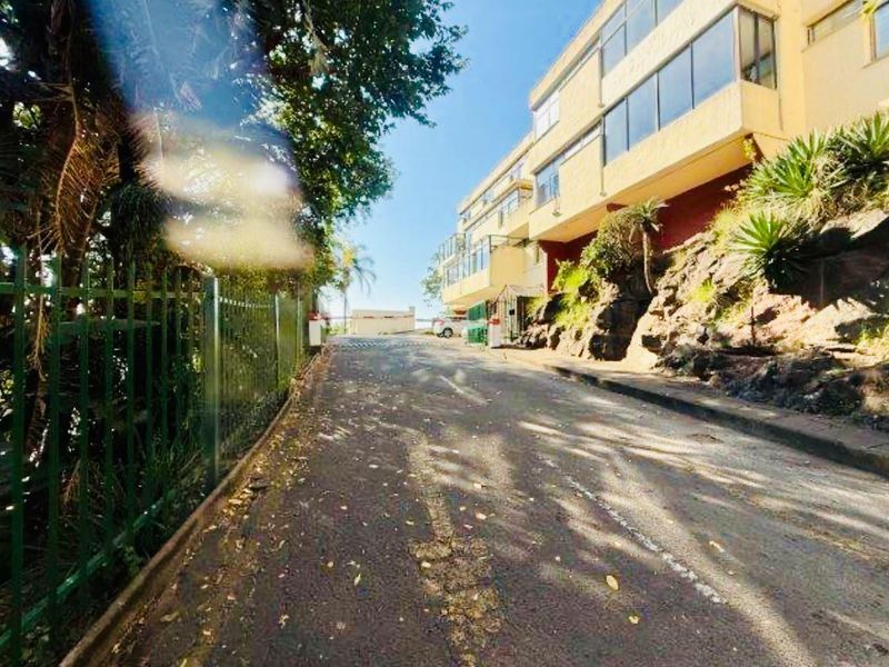 Street view showing the approach to the apartment complex with asphalt road, perimeter fencing, and building facade.