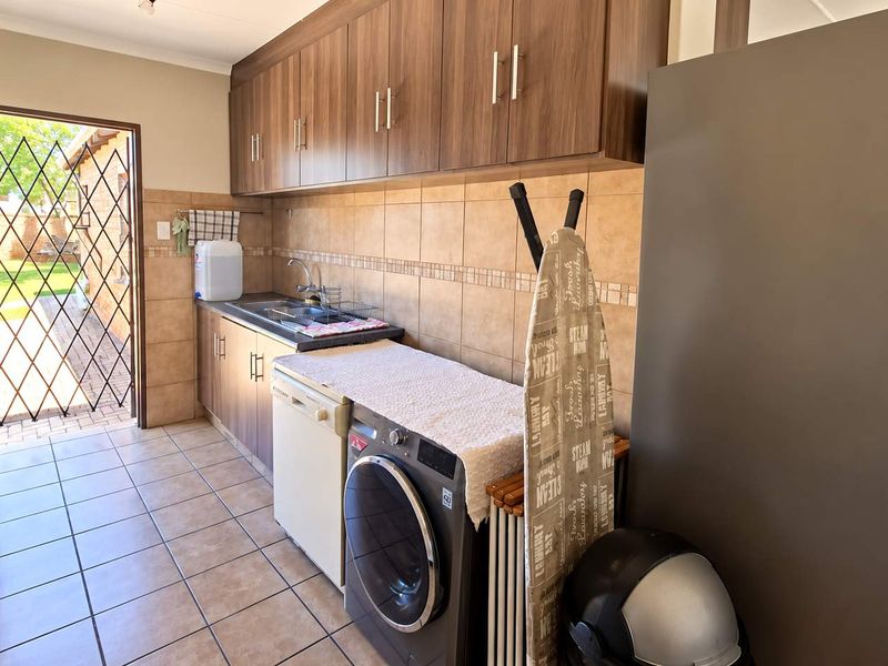 Functional laundry room featuring built-in wooden cabinetry, tiled backsplash, stainless steel sink, and direct access to the rear garden through a security gate.