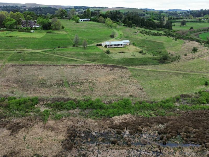 Aerial view of a large residential vacant land parcel featuring expansive green fields and an existing dwelling in a rural setting.