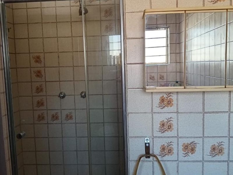 A dated bathroom featuring a glass shower enclosure, tiled walls with floral accents, and a wall-mounted medicine cabinet.