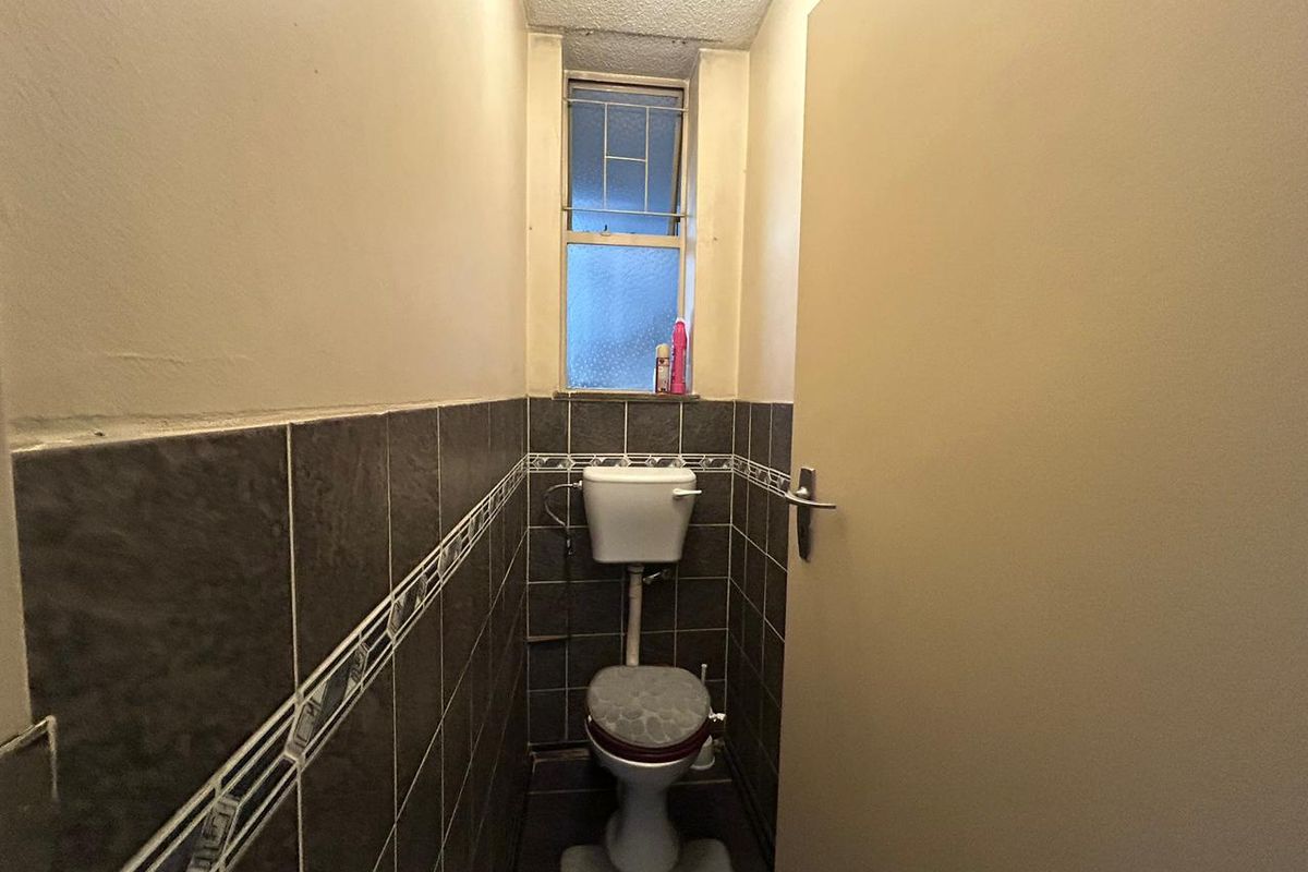 A compact, dated bathroom featuring dark wall tiles, a standard toilet, and a small window providing natural light.