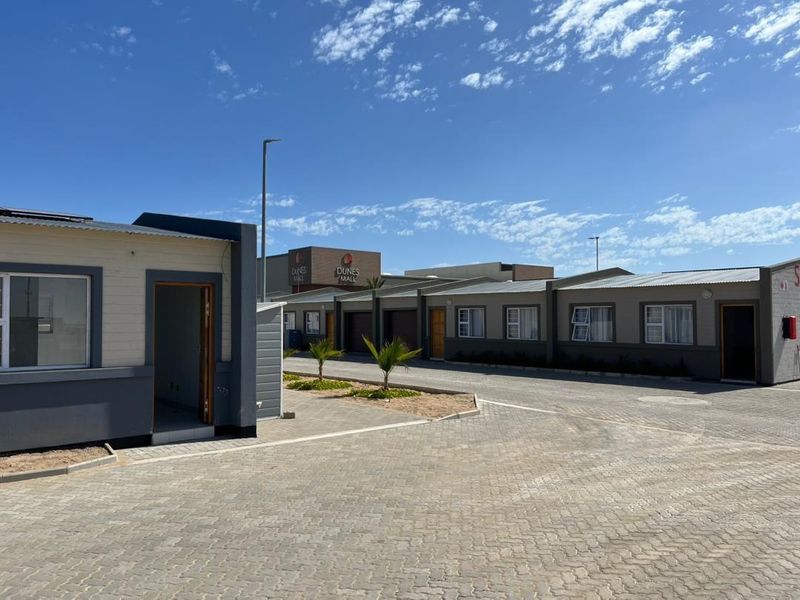Exterior view of a modern townhouse complex featuring paved driveways, corrugated metal roofing, and multiple unit entrances.