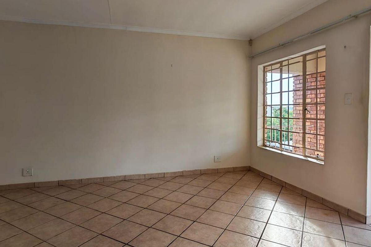 An empty bedroom featuring neutral tiled flooring, a ceiling light fixture, and a window fitted with security bars.