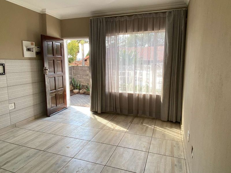 An empty living room featuring tiled flooring, a timber entrance door, and a large window providing natural light and access to the exterior.