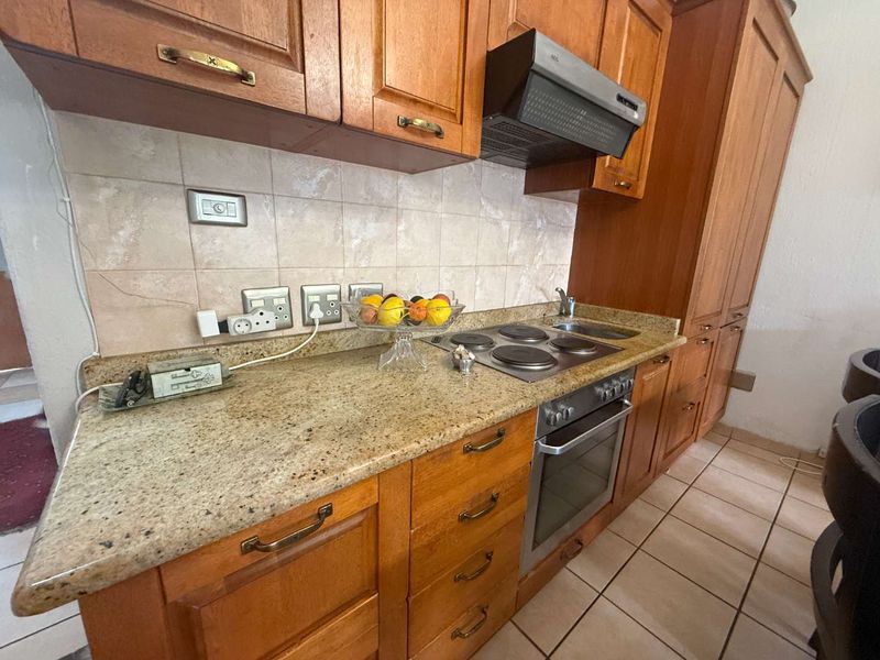 A functional kitchen featuring wooden cabinetry, granite countertops, built-in oven, electric hob, and tiled flooring, offering a classic layout with ample storage space.