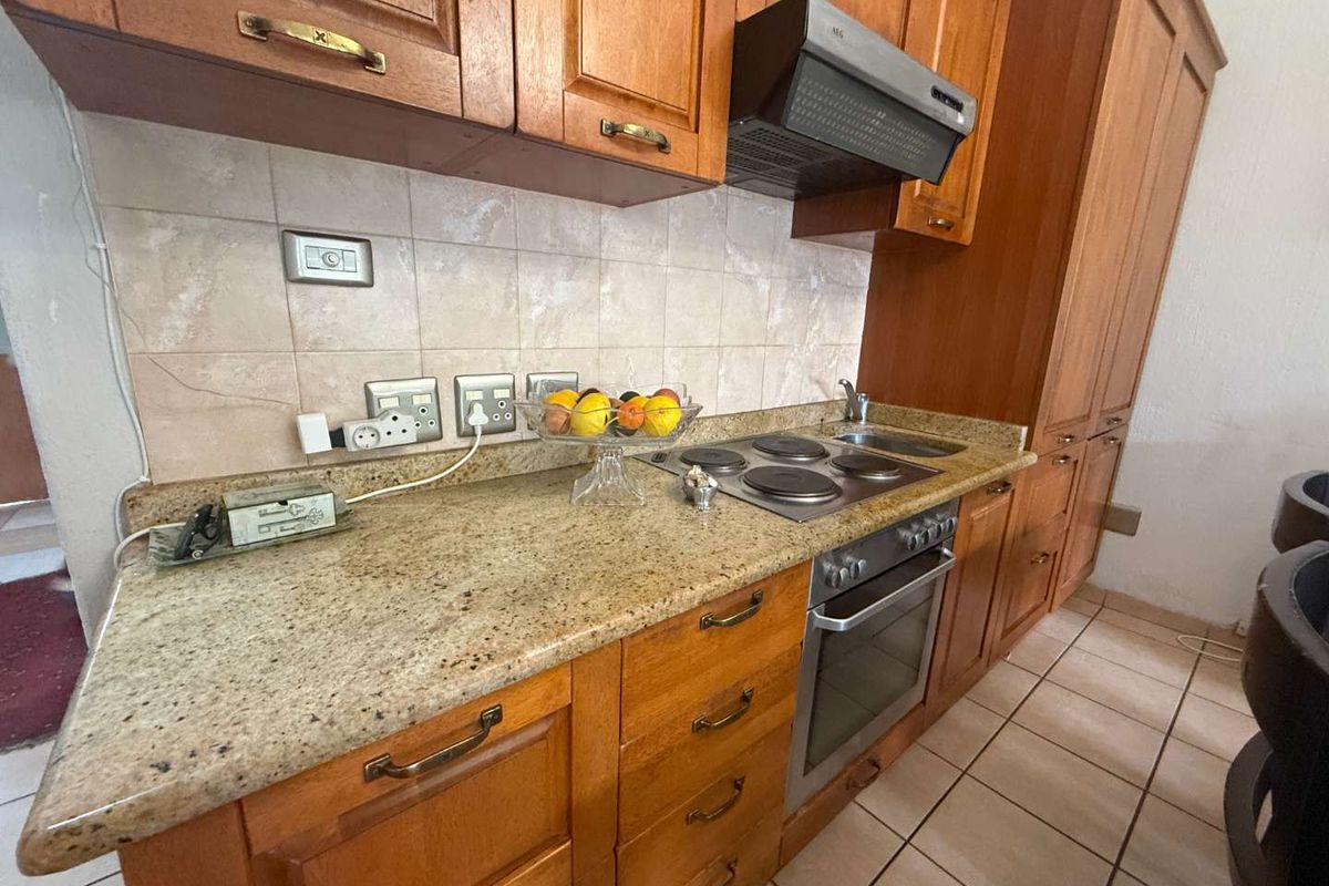 A functional kitchen featuring wooden cabinetry, granite countertops, built-in oven, electric hob, and tiled flooring, offering a classic layout with ample storage space.