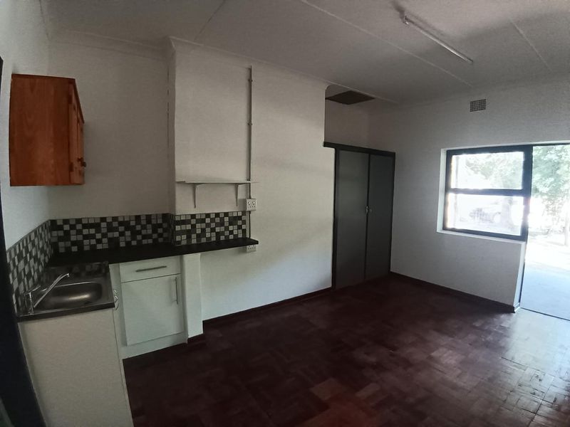 An open-plan living area featuring parquet flooring, a compact kitchen kitchenette with tiled backsplash, and built-in storage cupboards.