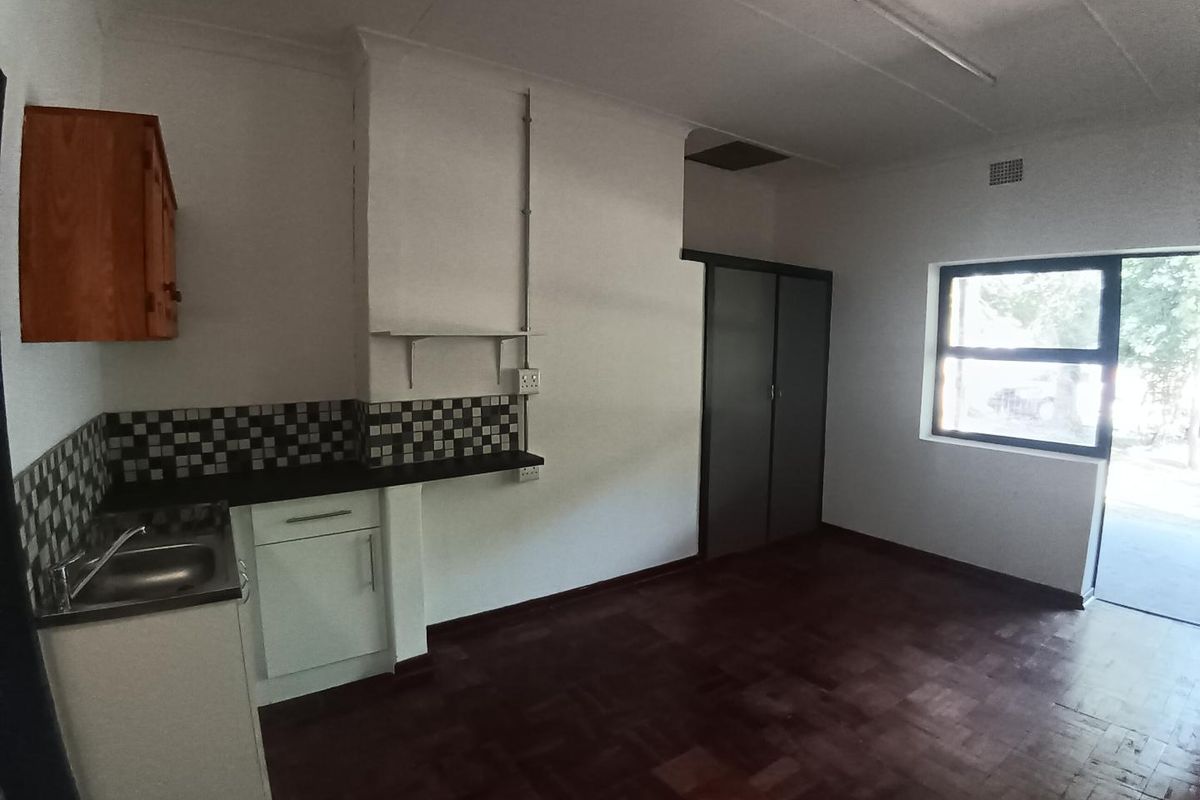 An open-plan living area featuring parquet flooring, a compact kitchen kitchenette with tiled backsplash, and built-in storage cupboards.