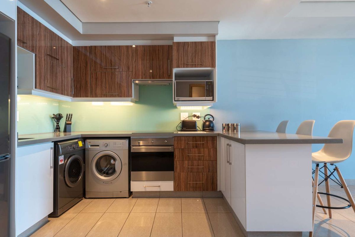 Modern kitchen featuring wood-grain cabinetry, stone countertops, integrated oven, hob, extractor fan, and built-in microwave, with a breakfast bar and tiled flooring.