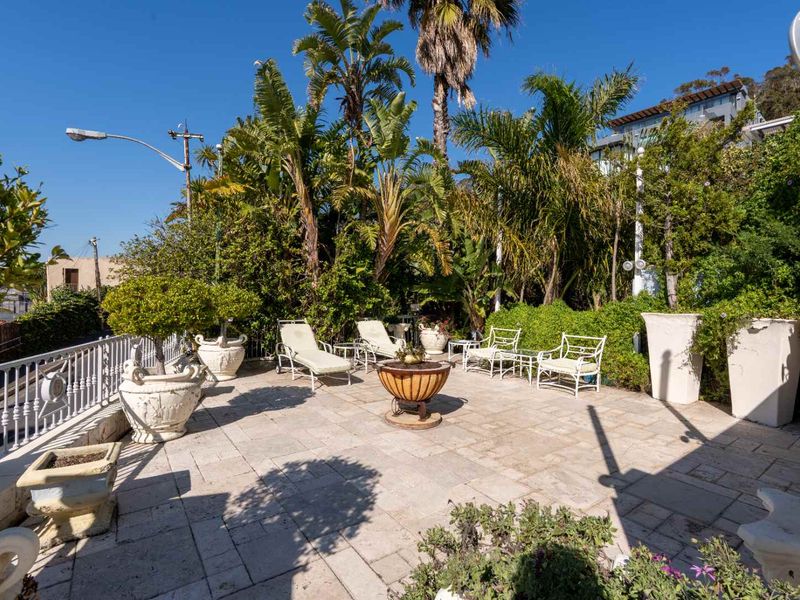 Spacious outdoor patio area featuring stone paving and a metal balustrade, surrounded by established garden greenery.
