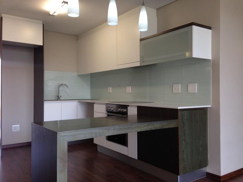 Modern kitchen featuring sleek white and dark wood cabinetry, integrated oven, cooktop, and a functional breakfast bar with a light-toned tiled backsplash.
