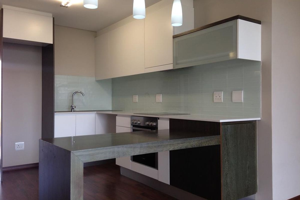 Modern kitchen featuring sleek white and dark wood cabinetry, integrated oven, cooktop, and a functional breakfast bar with a light-toned tiled backsplash.