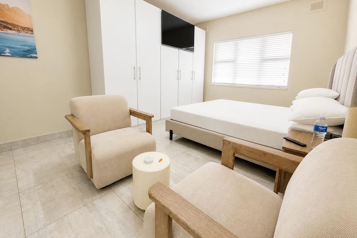 A well-maintained bedroom featuring neutral tiled flooring, built-in white cupboards, and venetian blinds, offering a clean and functional living space.