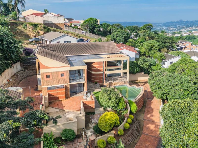 Aerial view of a multi-level residential property featuring a swimming pool, brick-paved outdoor areas, and tiered landscaping in a hillside setting.