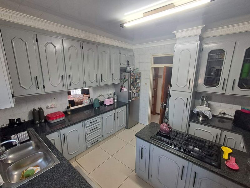 A functional kitchen featuring grey built-in cabinetry, granite countertops, a gas hob, and tiled flooring with classic coved ceiling detailing.