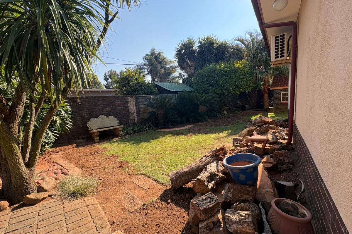 A rear garden area featuring a lawn, brick boundary wall, and exterior wall-mounted air conditioning unit.