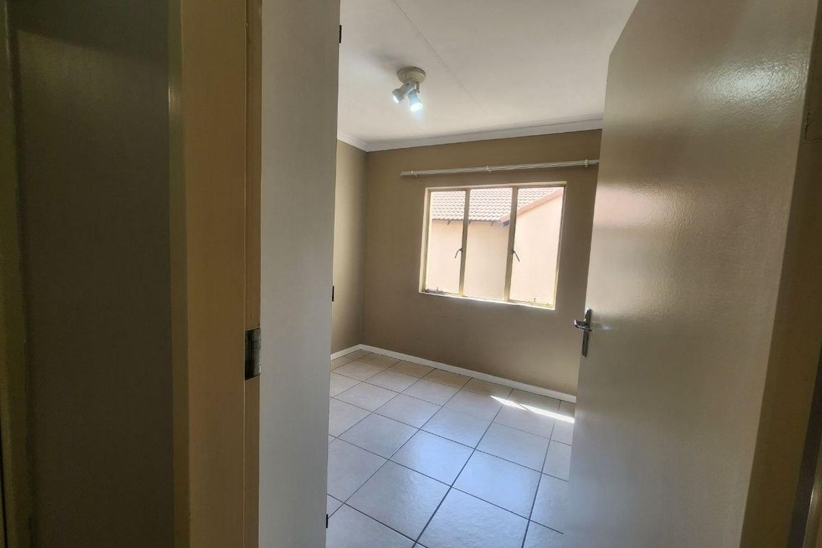 A vacant bedroom featuring neutral wall tones, tiled flooring, and a window with a fitted curtain rod.