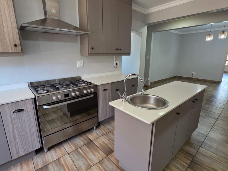 Modern kitchen featuring a gas stove, extractor fan, central island with a sink, and ample built-in cabinetry with stone countertops.