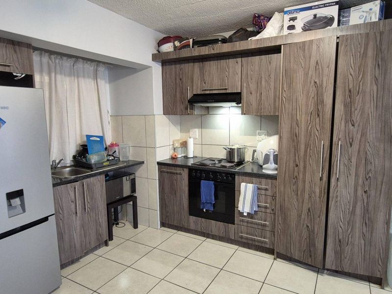 A functional kitchen featuring wood-grain cabinetry, built-in oven and hob, tiled backsplash, and tiled flooring, providing a practical workspace.