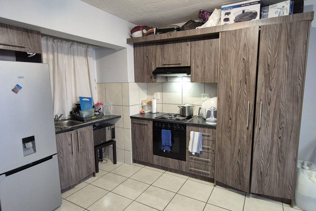 A functional kitchen featuring wood-grain cabinetry, built-in oven and hob, tiled backsplash, and tiled flooring, providing a practical workspace.