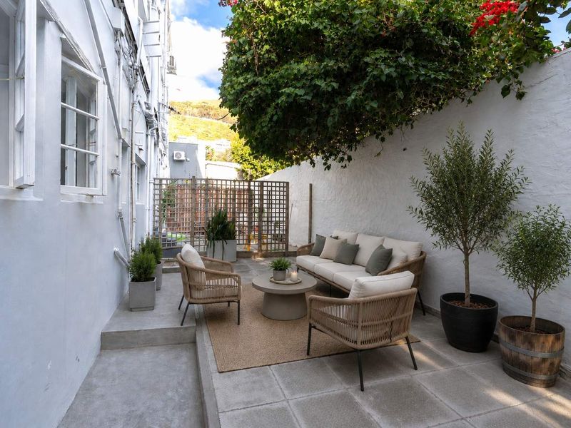 A private rear courtyard featuring a paved patio area, enclosed by a high boundary wall and timber lattice screening.