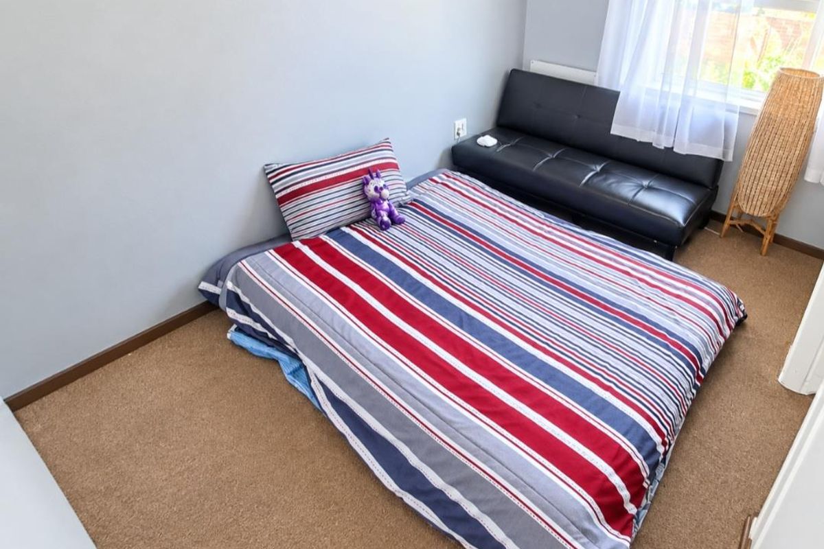 A simple bedroom featuring neutral wall paint, carpeted flooring, and a window allowing natural light into the space.