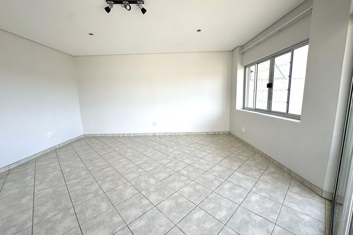 A bright, empty living room featuring neutral ceramic floor tiles, clean white walls, and a modern adjustable spotlight fixture.