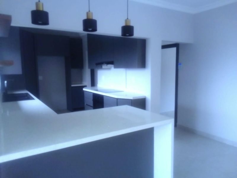 Modern kitchen featuring dark cabinetry, stone countertops, and contemporary pendant lighting in an open-plan layout.