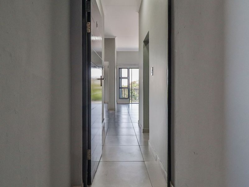 A bright, empty hallway with neutral walls and tiled flooring, leading towards an open living area with balcony access.